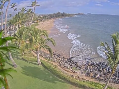 Kihei beach on Maui curving past a rocky point with palms on the live webcam