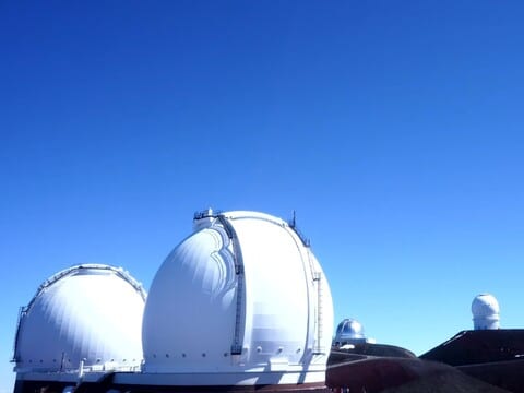 White observatory domes under a deep blue sky on the Mauna Kea summit on the live webcam